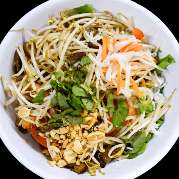 A vibrant vegan salad in a white bowl, topped with bean sprouts, herbs, and peanuts.