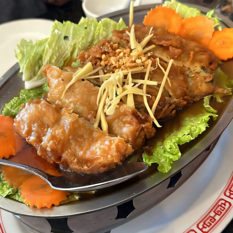 Vegan fried fish with ginger, peanuts, lettuce, and carved carrots in a savory sauce.
