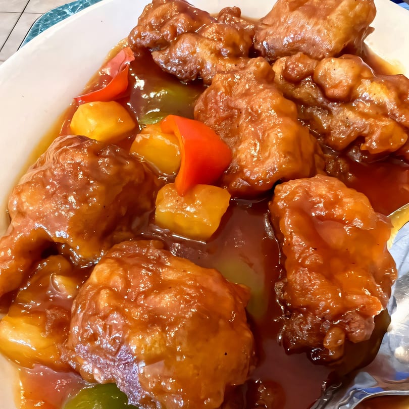 Sweet and sour vegan chicken with bell peppers and pineapple chunks in a white bowl.